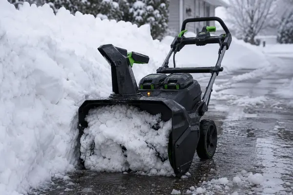 Black and green cordless snow blower stopped at a dense wet snowbank with an orange status indicator illuminated.