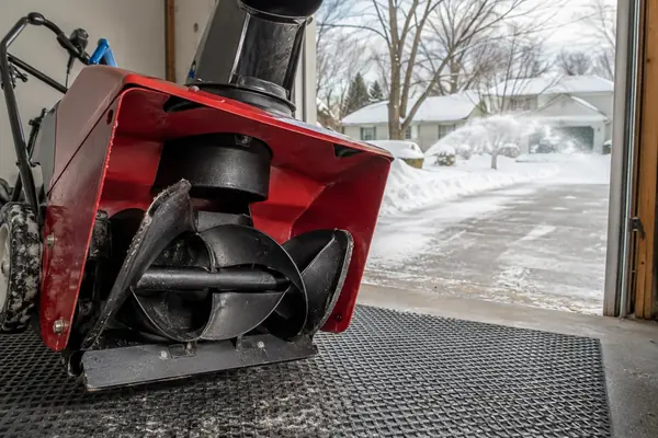 Red single-stage snow blower safely positioned for inspection of the rubber rotor blade and scraper area near an open garage.